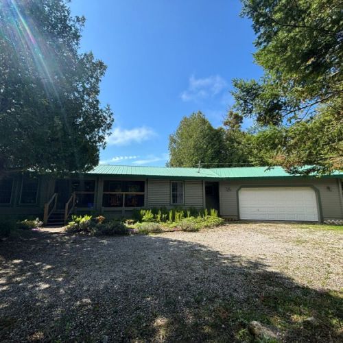 Peaceful woodland retreat with a bright green metal roof, wraparound porch, and private driveway—perfect for road trip getaways, nature escapes, and family vacations near the forest.