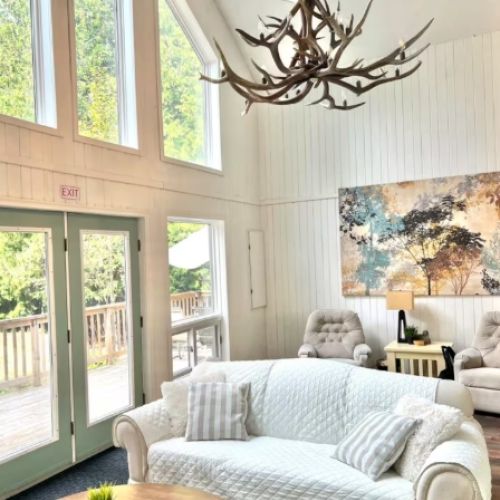 Soaring windows and soft, rustic decor create a bright and airy living space — perfect for morning coffee or unwinding after a day at the beach.