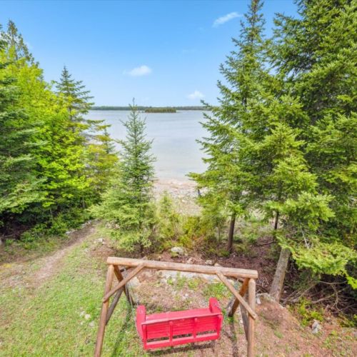 A charming red swing invites you to sit and sway while soaking up the peaceful view down to the bay.