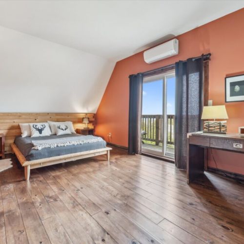 Spacious upper-level primary suite with a queen-size bed, wood accent wall, and private balcony access.