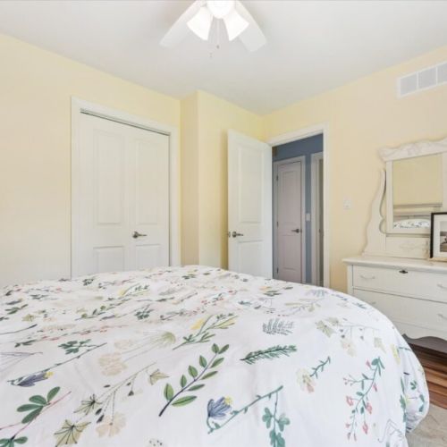 Charming bedroom with soft yellow walls, floral bedding, and a vintage white vanity dresser.