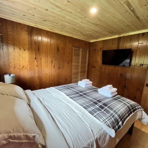 The minimalist and serene bedroom with queen bed, enclosed by wooden walls and a vaulted ceiling, giving that perfect cottage environment for a peaceful retreat.