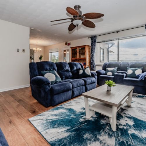Step into a bright and welcoming living room furnished with plush, deep-blue sofas designed for ultimate comfort. Large windows frame stunning lake views, flooding the room with natural light. The space is perfect for cozy evenings, whether you're curled up with a good book, watching TV, or simply enjoying the tranquil surroundings.