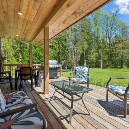 Unwind on the covered deck featuring comfortable seating, outdoor dining, and a BBQ—perfect for enjoying warm summer days rain or shine.