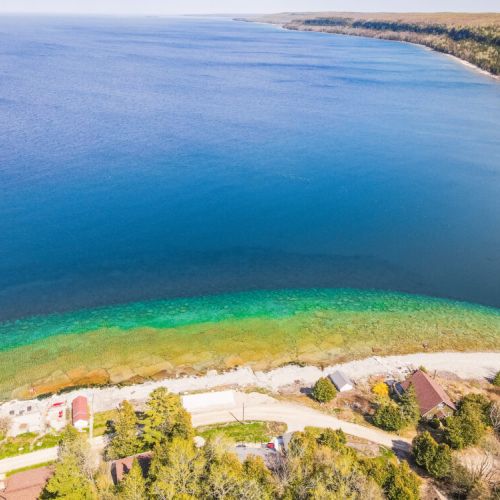Expansive aerial shot offering a mesmerizing view of the beautiful shoreline, with the serene, endless blue waters of the lake stretching out into the horizon. A perfect depiction of tranquility and natural beauty.