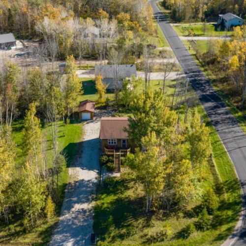 This stunning aerial view of Black Bear Cottage showcases its peaceful location nestled among mature trees and lush greenery. The property features a long driveway leading up to the cottage, with ample parking space and privacy, surrounded by nature.