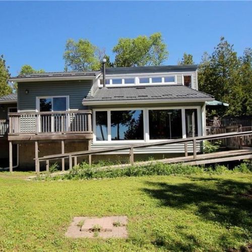 Spacious waterfront cottage with large windows and a sunny yard overlooking the lake.