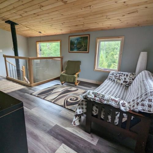 Relax upstairs in this cozy loft-style lounge featuring a wood stove, pine ceilings, and natural light—ideal for reading or quiet time.