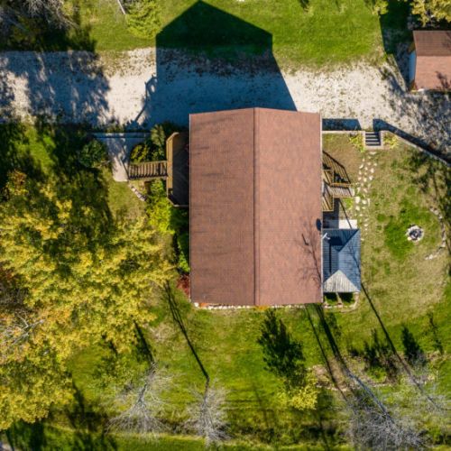 From above, the layout of the property is visible, with the cottage centrally located on a spacious lot. You can see the well-maintained yard, back deck, and fire pit, ideal for outdoor activities or simply relaxing in the serene environment.