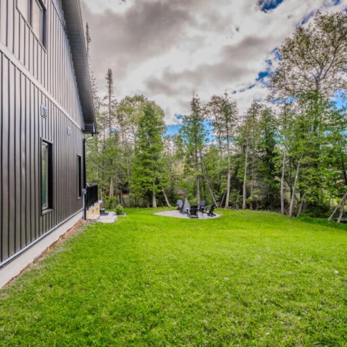 A wide lawn space leads to a fire pit, perfect for gatherings, offering peace and tranquility in a forested setting.