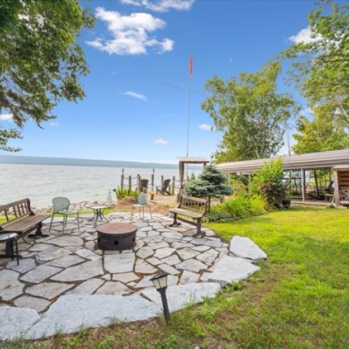Scenic lakeside fire pit area with stone patio, ample seating, and stunning waterfront views—perfect for cozy evenings outdoors.
