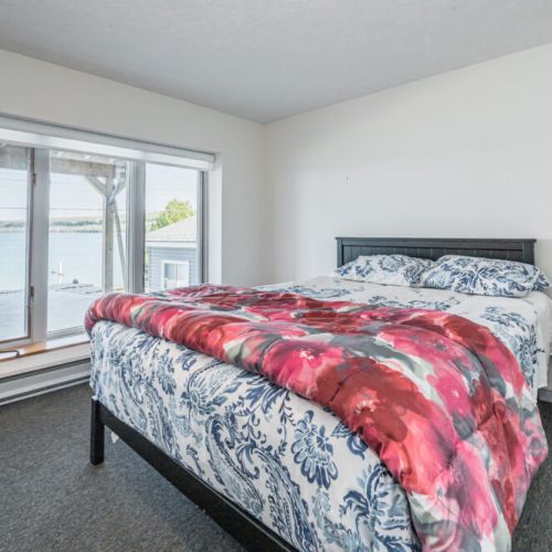 Cozy and inviting bedroom featuring a vibrant, patterned comforter. The large window provides an unobstructed view of the tranquil lake, ensuring you wake up to the beauty of nature every morning.