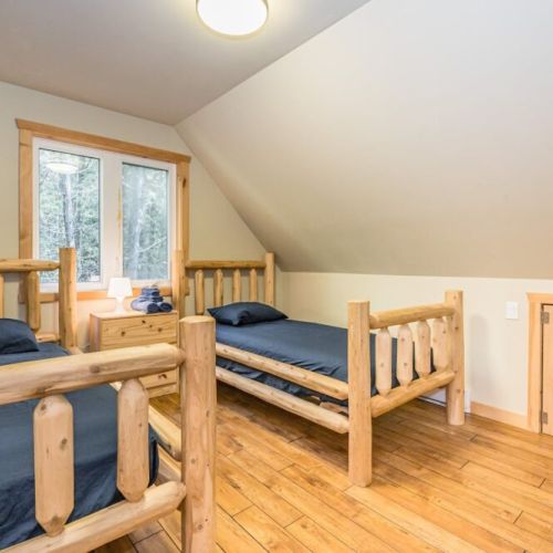 Two single beds on the upper level bedroom. Twin beds crafted from natural wood stand ready, offering a simple, restful environment for guests after a day of exploring.