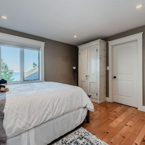 Bright bedroom with a stunning water view, featuring a cozy bed and rustic armoire—offering a tranquil and inviting atmosphere.