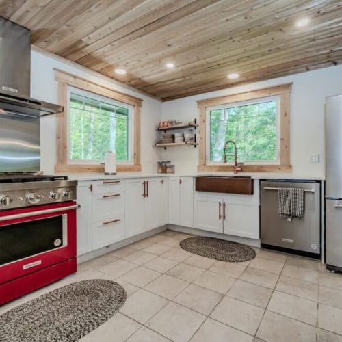 Cook with a view! This fully-equipped kitchen features large awning windows, a bold red stove, and everything you need for meals at home..