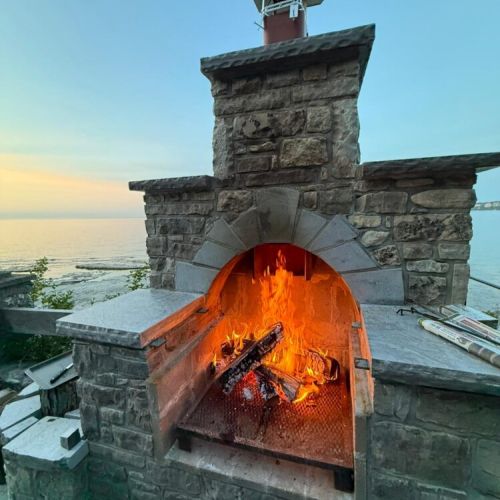 Evening glow at Lions Den Cottage: The wood-fired outdoor stone oven blazing as the sun sets over the lake.