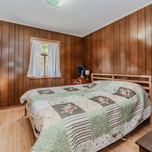 Rest easy in a cozy bedroom with rustic wood walls and a comfy queen bed—perfect for peaceful nights during your countryside getaway or cottage vacation.