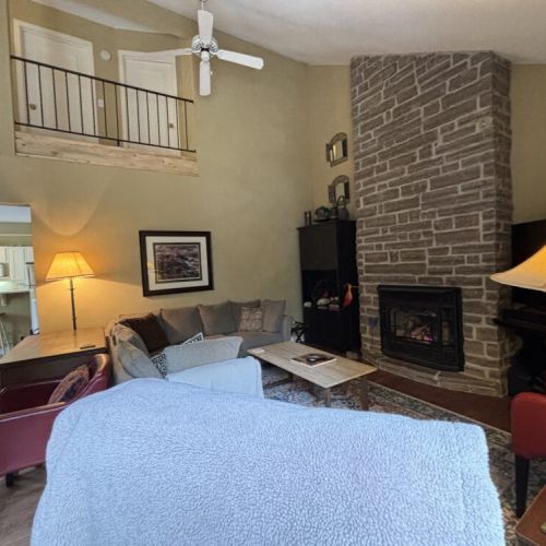 Warm Hearth and Home: This photo centers on the heart of the living area—the inviting stone fireplace. Its classic design and the glow of a fire offer a timeless charm that radiates throughout the space, providing a cozy place for guests to gather, share stories, or simply enjoy a peaceful evening in.
