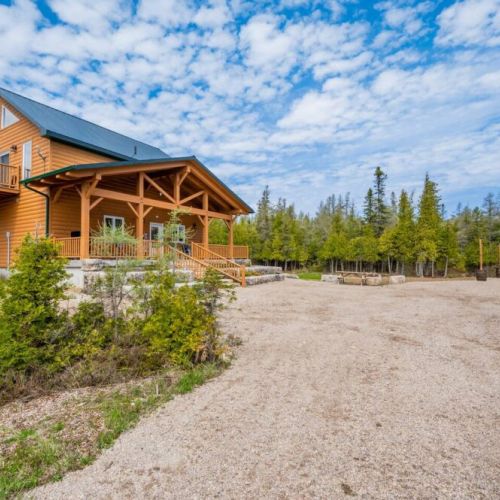 Saw N' LogzzZ showcases its impressive structure and beautifully landscaped front yard, offering a warm and inviting entrance.