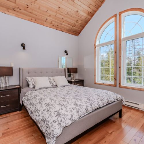 Stunning master suite with grand arched windows, vaulted ceiling, and forest views—your private haven for rest and relaxation.