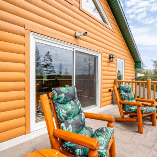 The balcony features handcrafted log chairs with plush cushions, creating an inviting space to relax and soak in the serene views of the forest.