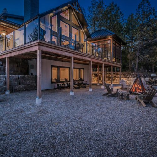 Experience lakeside luxury at this modern vacation rental featuring panoramic windows, a cozy fire pit lounge, and elevated outdoor living—ideal for relaxing getaways, cottage escapes, and memorable travel adventures in nature.