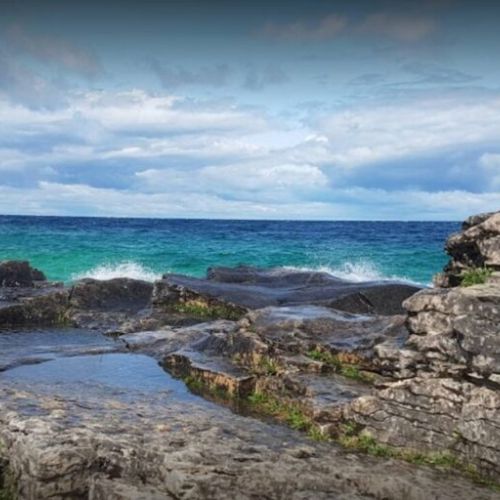 A breathtaking view of the rugged Bruce Peninsula coastline, showcasing the crystal-clear turquoise waters of Lake Huron. This stunning natural beauty is just a short drive away.