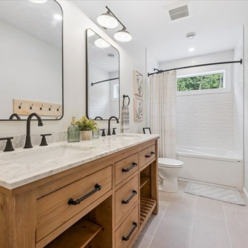 Modern meets rustic in this stylish bathroom, featuring a double vanity with natural wood, matte black fixtures, and a bright tub-shower combo framed by crisp tilework.
