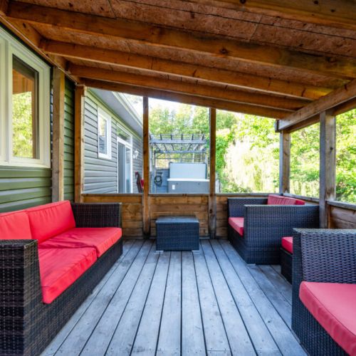 Relax in style on the covered deck with cozy red-cushioned patio seating—perfect for evening chats or morning coffee at this serene vacation rental retreat.
