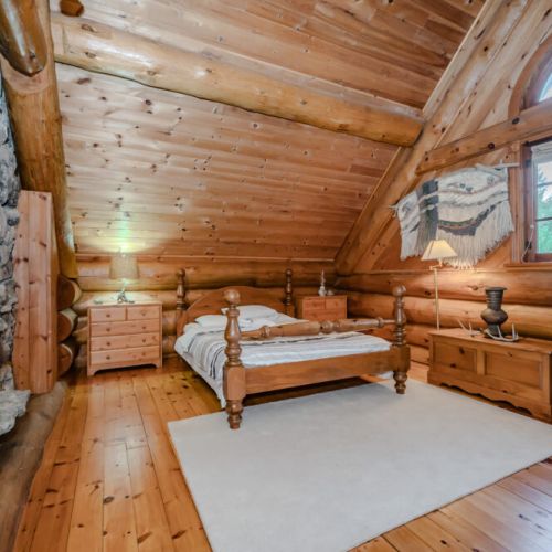 A beautifully designed loft bedroom with vaulted ceilings and natural light pouring in through large windows. The rustic charm of the wood detailing ensures a relaxing retreat.