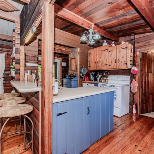 Cook up comfort in this rustic log cabin vacation rental featuring a charming full kitchen, cozy bar seating, and warm wood finishes—perfect for culinary adventures during your relaxing family retreat or countryside getaway.