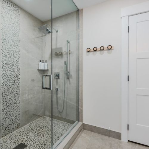 The walk-in shower is a standout feature with its chic, pebble-tile accent and glass doors. Equipped with modern fixtures, it offers a spa-like experience for guests.
