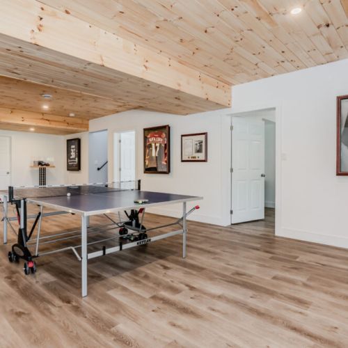 Enjoy some friendly competition in our spacious recreational area, complete with a ping pong table and surrounded by framed sports memorabilia. This inviting space, with its wooden ceiling and ample lighting, is ideal for family fun and games.