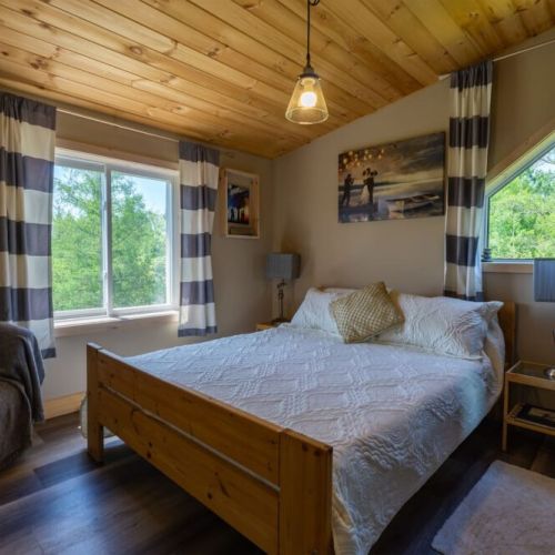 Wake up to peaceful forest views in this tranquil cabin-style bedroom with vaulted ceilings, warm lighting, and modern cottage charm.