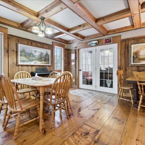 Cozy dining area with pine floors and French doors leading to the wrap-around porch, perfect for shared meals and easy indoor–outdoor living.