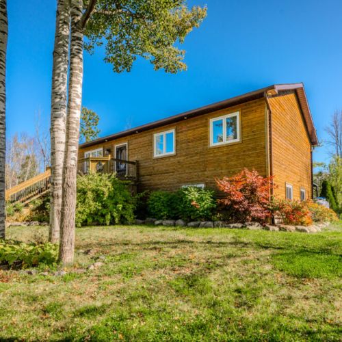 A charming log cabin-style exterior surrounded by nature, with large windows and a welcoming front deck.