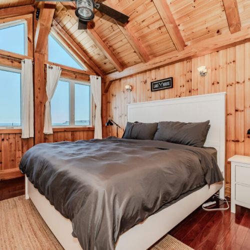 Stunning master bedroom with vaulted ceilings, panoramic lake views, and cozy wood finishes—perfect for romantic escapes or restful retreats.