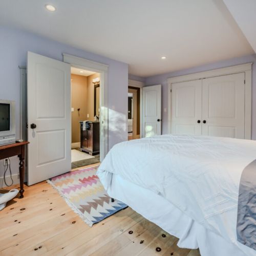 A bright and airy bedroom with a plush bed and access to an ensuite bathroom, featuring wooden flooring and natural lighting.