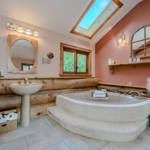 This elegant bathroom features a luxurious whirlpool tub, skylight for natural light, and rustic log detailing, creating a relaxing oasis with a touch of modern sophistication.
