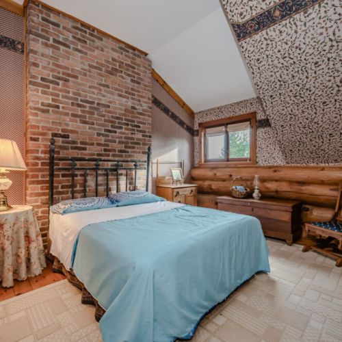 A cozy bedroom with a stunning brick accent wall and vaulted ceiling exudes rustic elegance. The tranquil atmosphere and warm textures make this a restful retreat.