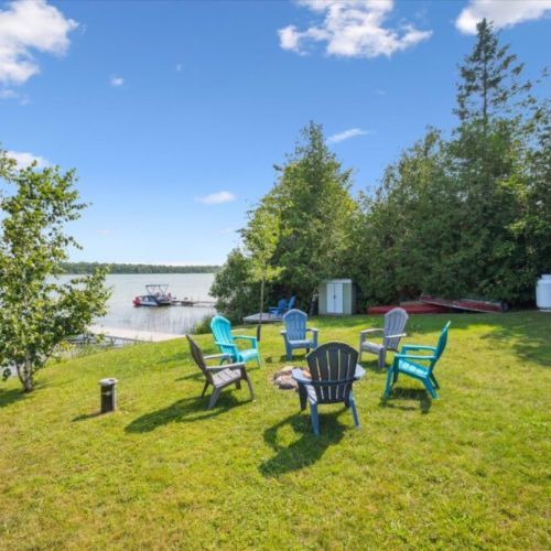 Lakeside fire pit area with colorful Adirondack chairs, perfect for gathering with friends and family while enjoying beautiful waterfront views and easy access to the private dock.