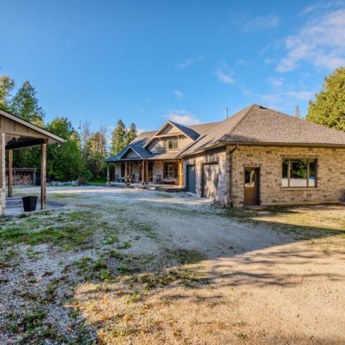 A spacious property featuring a rustic exterior, a separate building, and a gravel driveway, surrounded by greenery and trees, offering a peaceful and private setting.
