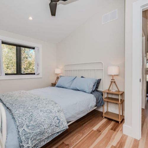 Bright and airy bedroom with natural wood floors and cozy bedding, offering a peaceful retreat in a tranquil forest setting—perfect for a restful vacation rental stay near the lake.