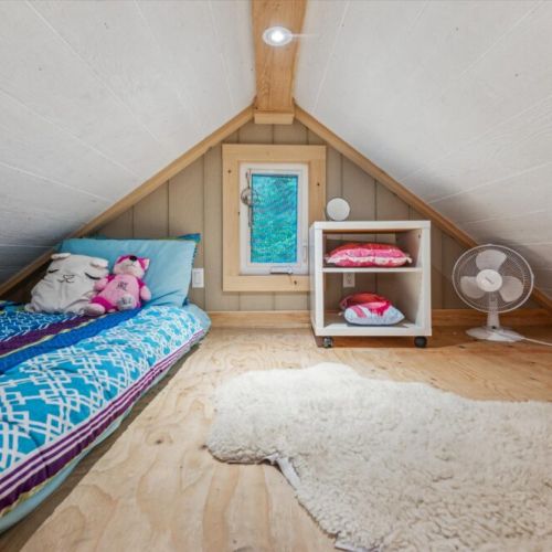 Nestled under the eaves, the cozy loft space is a favourite for kids and adventurous guests. With its angled ceiling, colorful bedding, and woodland window view, it's like sleeping in a storybook.