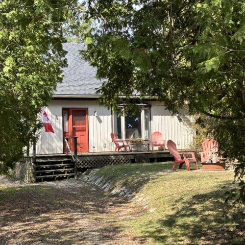 Rustic Cottage Exterior: The exterior of The Louise exudes classic cottage charm, set against the backdrop of lush greenery. The Canadian flag proudly displayed adds a touch of patriotism, while the red Adirondack chairs on the porch invite guests to sit back and soak in the tranquility of cottage country.