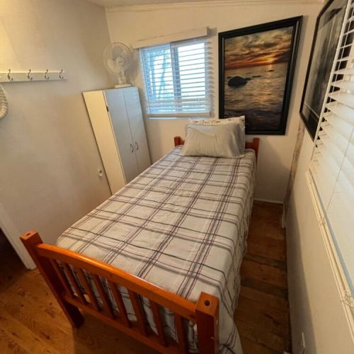 This charming single bedroom offers a peaceful and private space, perfect for solo travelers or kids. Featuring a classic wooden bed frame, soft linens, and warm cottage decor, it provides a comfortable night's sleep. Large windows let in natural light and offer a refreshing breeze, while the beautiful lake-themed artwork adds a relaxing touch. A wardrobe and wall hooks provide convenient storage for your stay.
