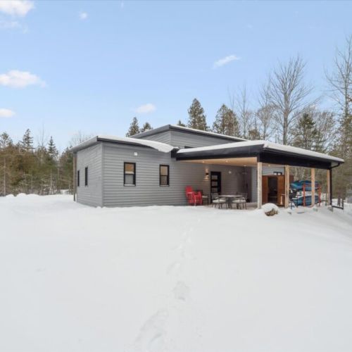 Winter exterior view of the cottage with covered patio, outdoor seating, and peaceful forest surroundings.