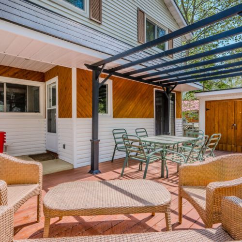 The back patio includes a cozy seating area with wicker chairs and a matching table. A BBQ grill is conveniently located nearby, ideal for summer cookouts.