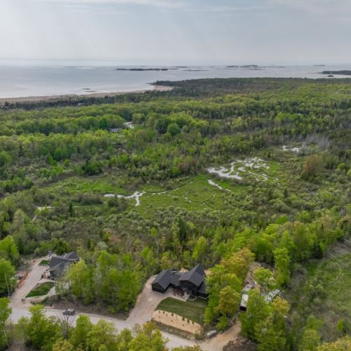 A view of the cabin and its surrounding landscape, including lush forests and a glimpse of nearby water bodies. It's an ideal setting for those seeking tranquility and natural beauty.