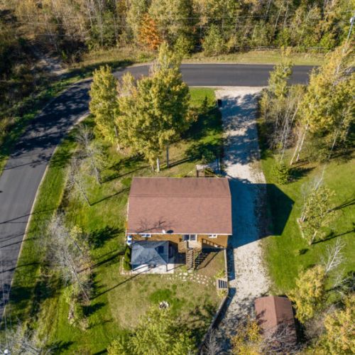 This side view highlights the cottage’s proximity to the quiet country road and surrounding homes, while still offering a private retreat. The nearby trees provide a natural barrier and enhance the peaceful, secluded atmosphere of the property.